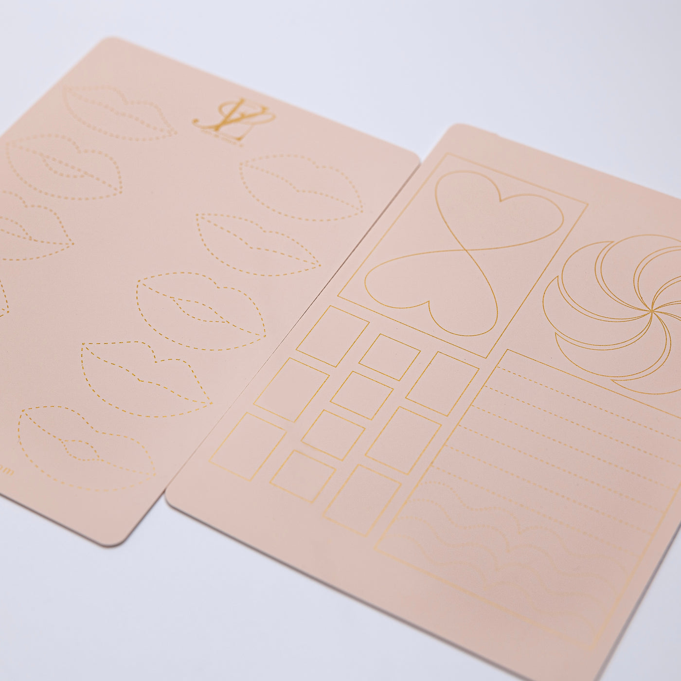 Two sheets of light pink paper with various golden line illustrations, including lips, hearts, squares, and wavy lines, arranged symmetrically on a light background. Perfect for enthusiasts of LIP PRACTICE PADS EXCLUSIVELY MADE BY ESPOIR STUDIOS by Espoir Studios.