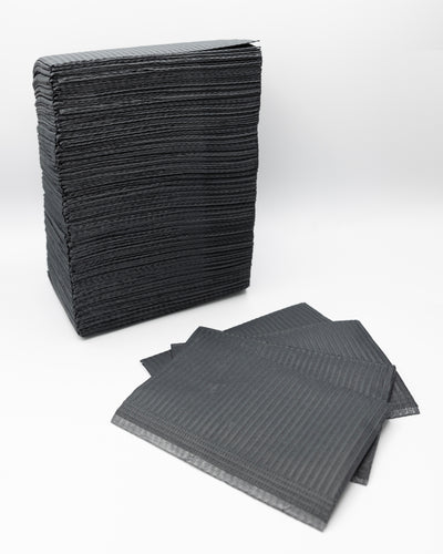 A stack of Espoir Studios disposable black rubber mats suitable for DISPOSABLE DENTAL BIBS (125 pieces) or PMU procedures on a white surface.