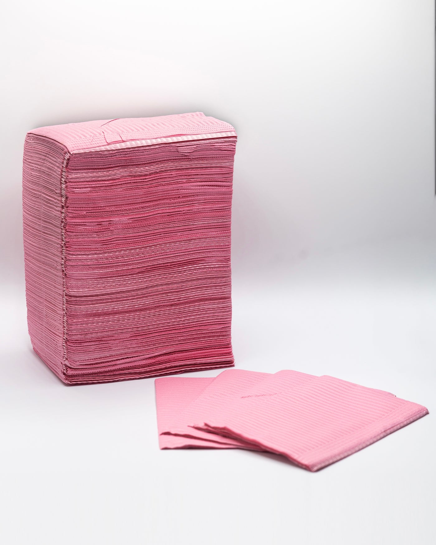 A stack of Espoir Studios' Disposable Dental Bibs (125 pieces) on a white surface.