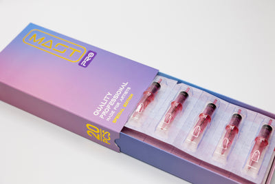 A purple and blue box labeled "MAST PRO SE UNIVERSAL NEEDLE CARTRIDGE (Round Shader - RS)" by Dragonhawk containing 20 professional disposable tattoo cartridges with five visible cartridges filled with pink ink.